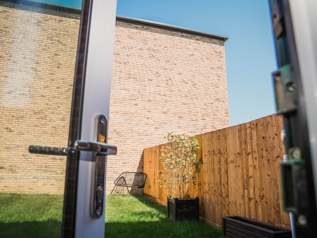 Private rear garden at The Buckingham, featuring a lawn, timber fencing, planted tree and patio access through glazed doors.
