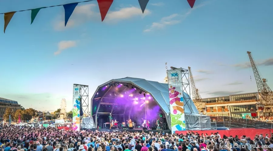 Bristol Harbour Festival music festival with a large crowd watching a band performing on a colourful stage during clear evening skies.