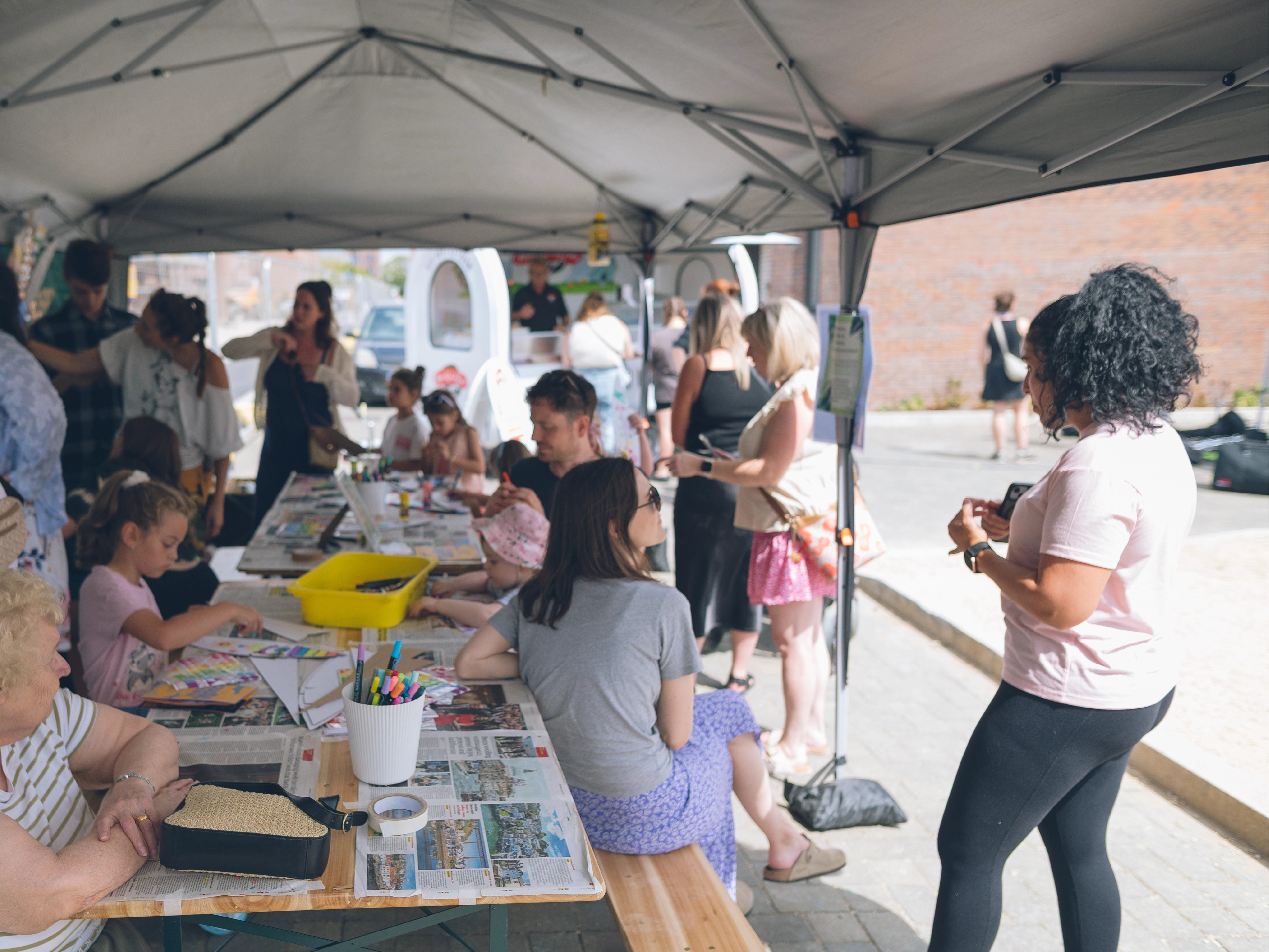 A community art workshop at Brabazon. Adults and children engaging in crafts at tables under a canopy. 