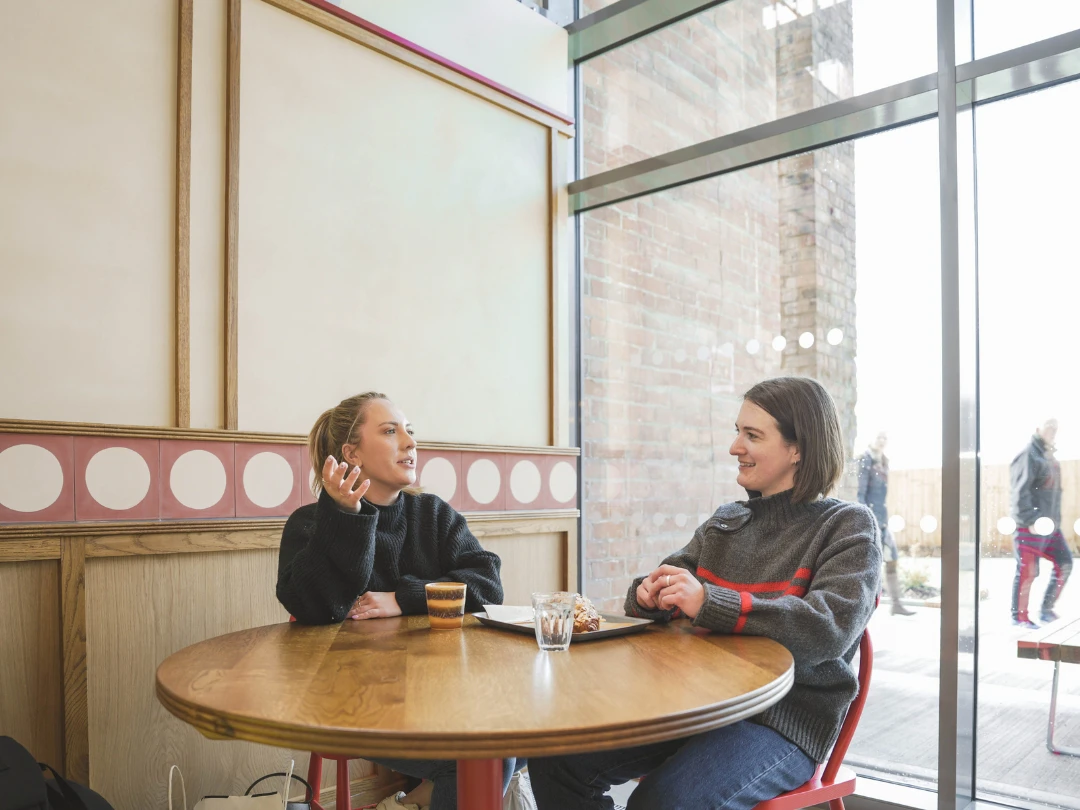 Two people in conversation at a table with a coffee and pastry