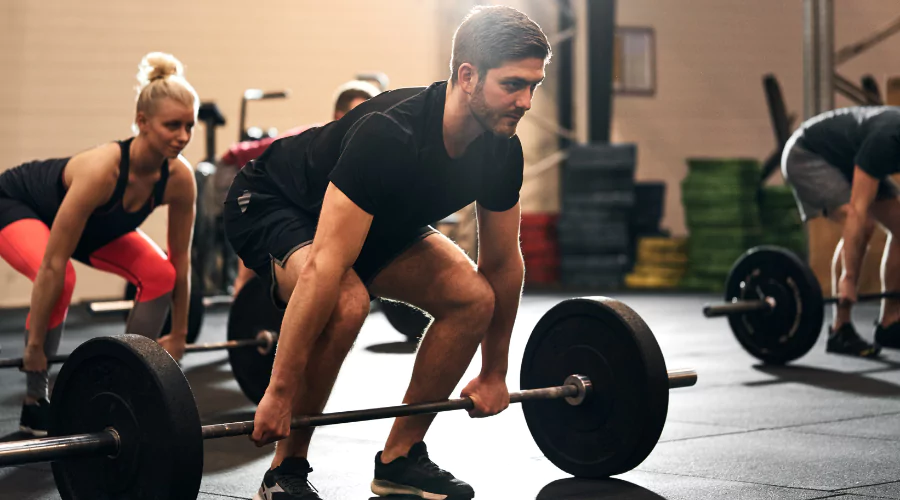 Small group strength class with focus on male in black active wear preparing for a deadlift.