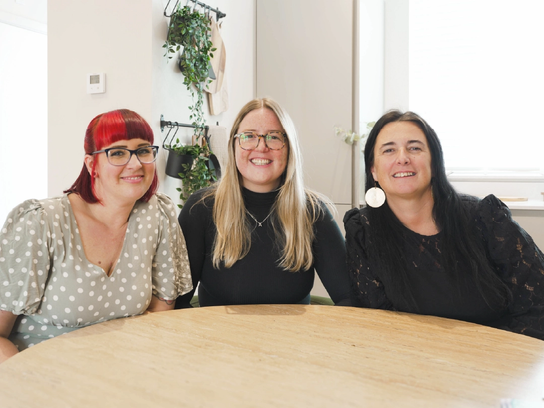 Three members of the Customer Relations Team at YTL Developments sitting at a wooden table inside a home at Brabazon. 