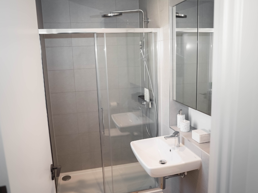Contemporary en-suite bathroom in a home at Brabazon, featuring a walk-in shower, wall-mounted basin, mirrored storage cabinet and large-format grey wall tiles.