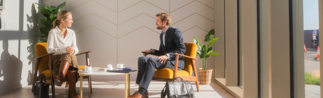 A man and a woman sit in armchairs in a sunlit office in Brabazon, engaged in conversation. 