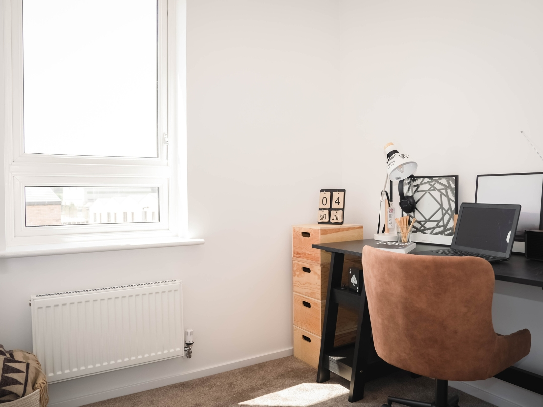 Dedicated home office space in The Buckingham, featuring long window, table and carpet flooring. 