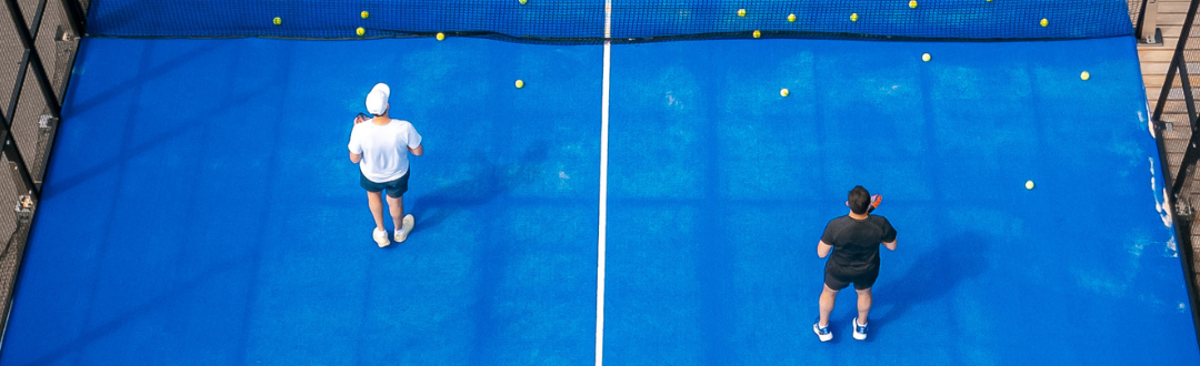 Two men pictured from above dressed in sports clothing on a padel court ready to play padel.