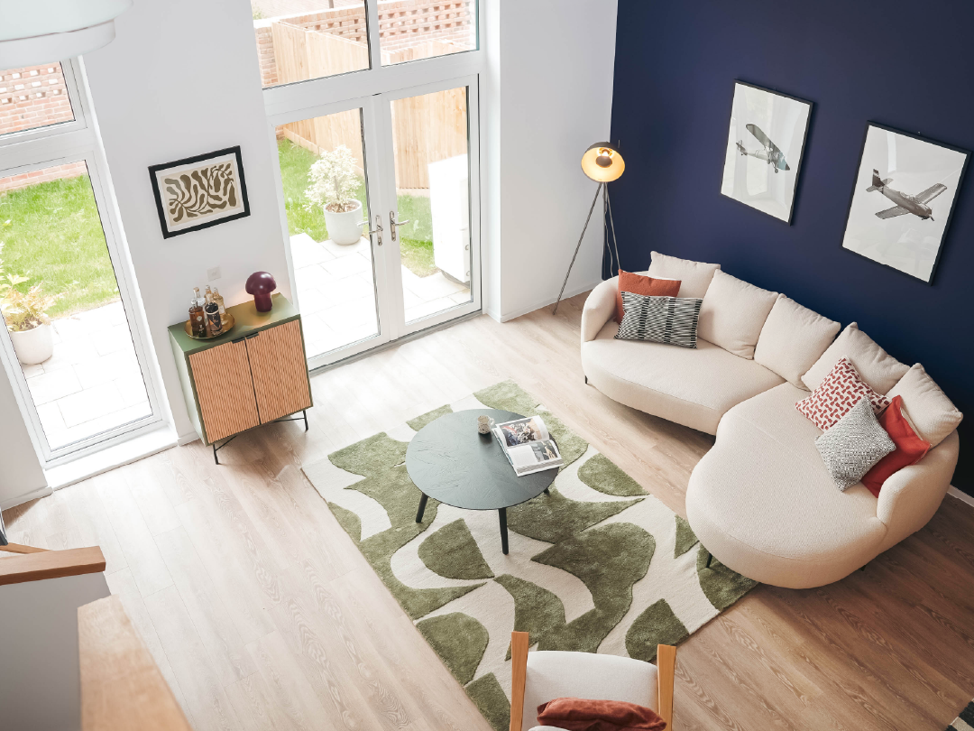Modern living room inside The Skylark Show Home, with curved beige sofa, patterned rug, round coffee table, navy accent wall, and large French doors opening to a garden.