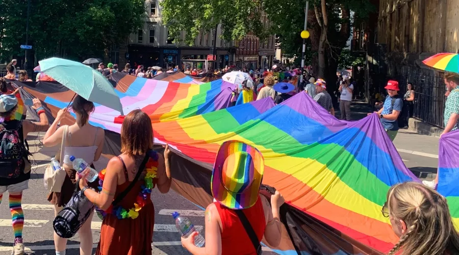 Crowd carrying a large rainbow pride flag during Bristol Pride parade on Baldwin Street, Bristol. 