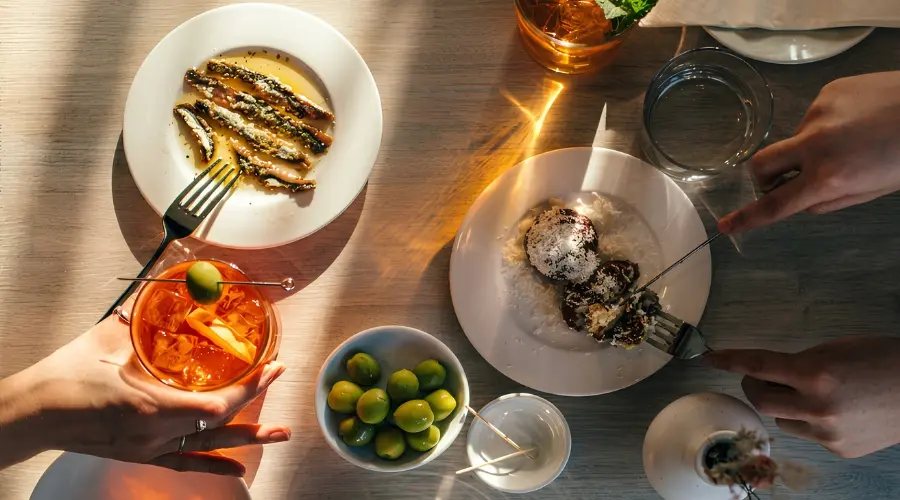 Overhead view of small plates, olives and cocktails being enjoyed at a restaurant table.