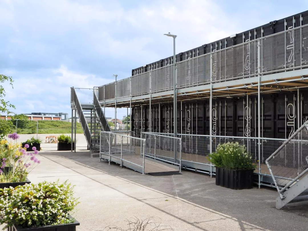 Boxworks' industrial black shipping container offices on a sunny day at Brabazon in Bristol with external metal stairs railing and planting.