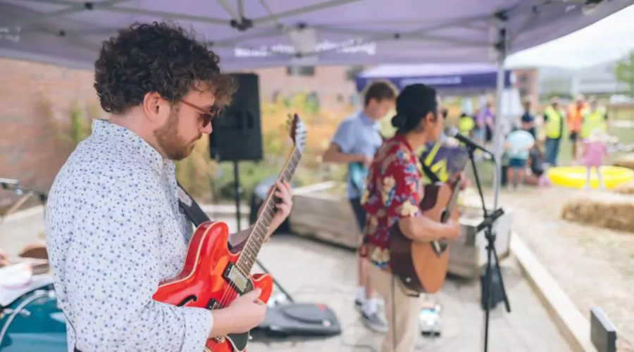 A musician plays a red guitar at outdoor event at Brabazon, accompanied by another artist with an acoustic guitar, performing outdoors at a lively event.