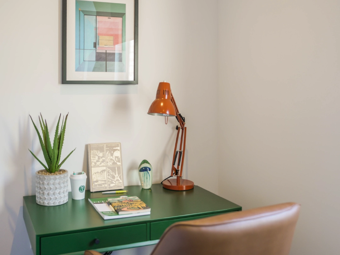 Green desk with potted plant, orange lamp and leather chair in secluded study in The Burney at Brabazon. 