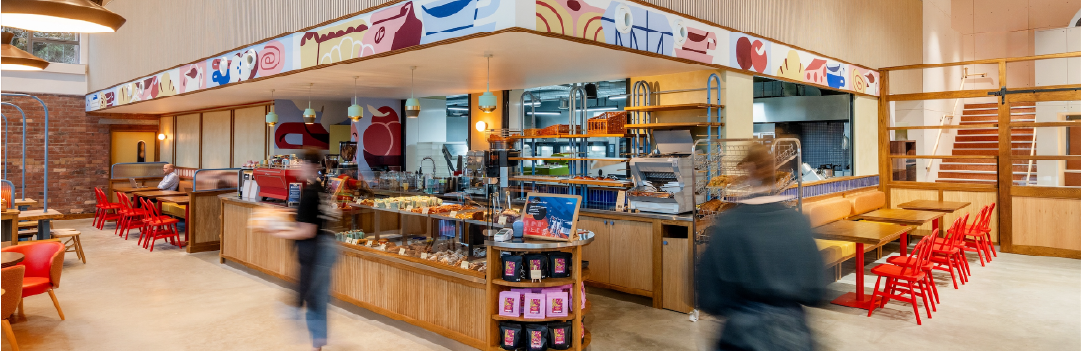 Mokoko Bakery at Brabazon: a bright café with a modern vibe, featuring colourful mural art above a wooden counter displaying pastries. Red chairs and tables line the seating area.