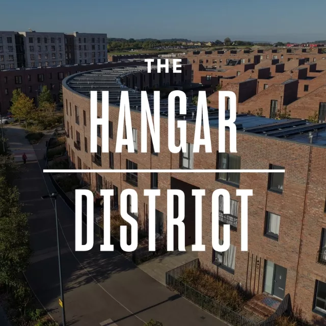 Aerial view of "The Hangar District" featuring modern, curved brick homes with solar panels on rooftops, set against a clear blue sky.