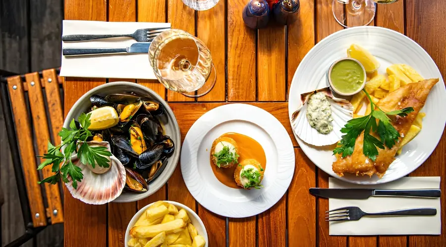 Overhead view of seafood dishes, chips and drinks served on a wooden restaurant table.
