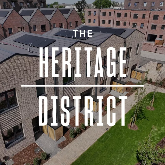 Aerial view of modern brick townhouses at Brabazon with solar panels, surrounded by landscaped gardens and pathways. Text overlay reads "The Heritage District."