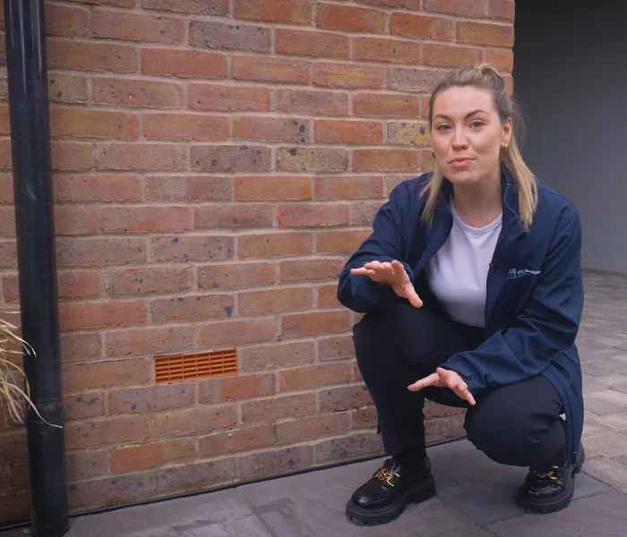 Young female crouching in front of a house air vent